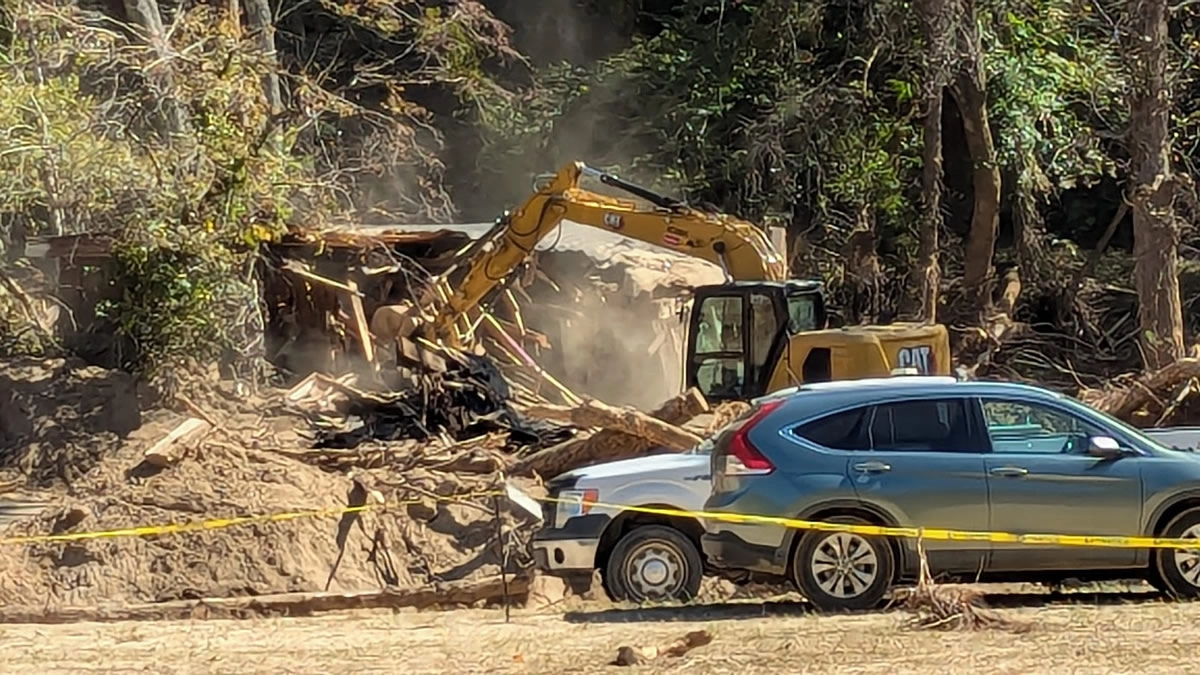 Heavy machinery razing the remains of a cabin destroyed by Hurricane Helene in Green River Cove