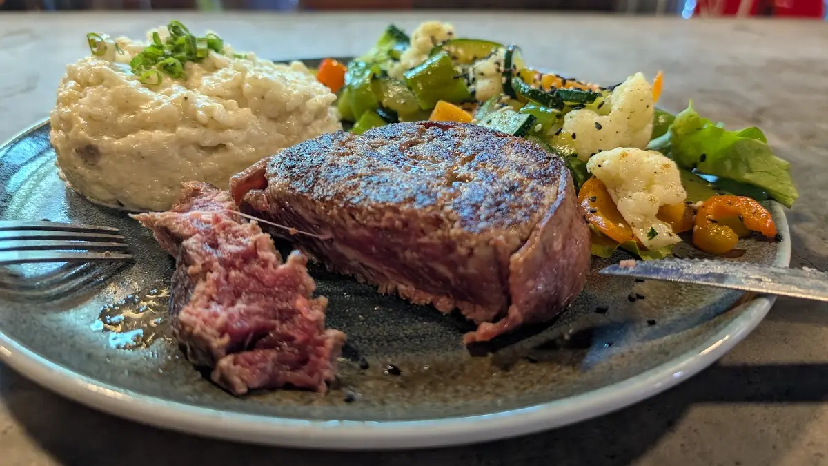 A blue rare steak served with mashed potatoes and mixed vegetables in Ecuador