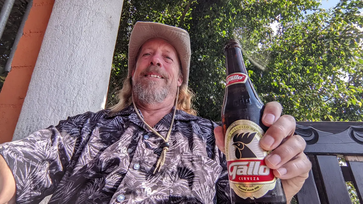 Fast Fred Ruddock enjoying a local Gallo beer at Lake Atitlán, Guatemala, reflecting the 'follow the smoke and the locals' travel philosophy.