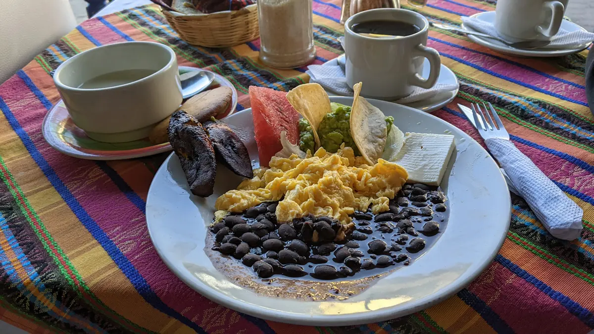 A traditional Guatemalan breakfast (Desayuno Chapín) featuring eggs, black beans, plantains, and tortillas, illustrating high-value local dining.