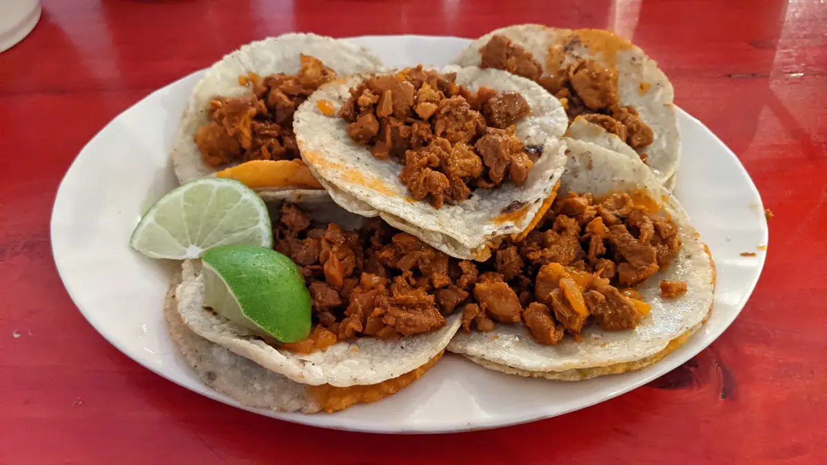 Authentic Tacos al Pastor featuring marinated pork shaved from a traditional trompo, topped with pineapple, cilantro, and onions.