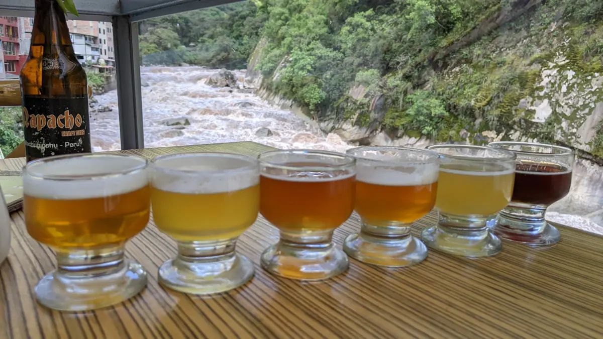 Craft beer samples in foreground and the raging Urubamba River in the background at Aguas Calientes Peru during early rainy season.