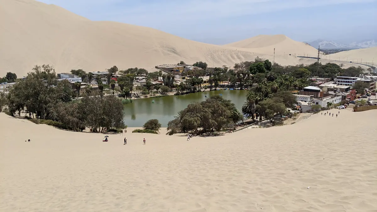 Overlooking the desert oasis of Huacachina with its green lagoon, palm trees, and surrounding village nestled among massive sand dunes in Peru.